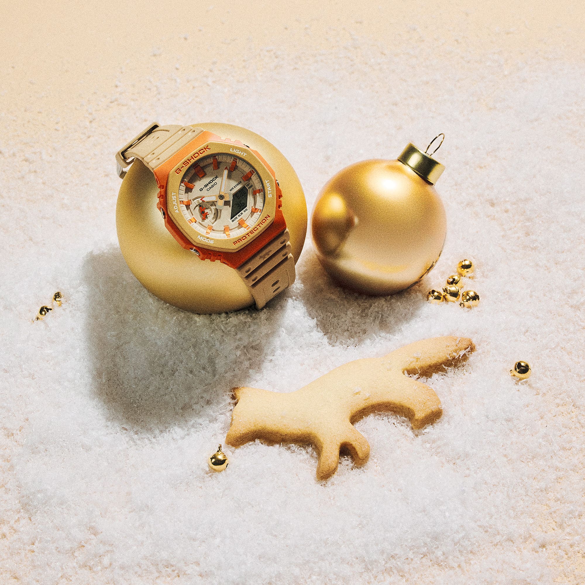 The G-SHOCK and Maison Kitsuné collaboration watch in beige and orange on a golden Christmas bauble. Link to the collaboration landing page.