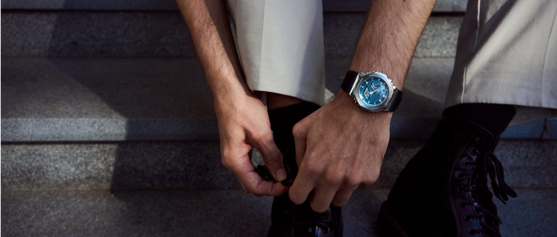 A man ties his shoelaces and wears the GBM-2100A-2B with a bright blue dial.