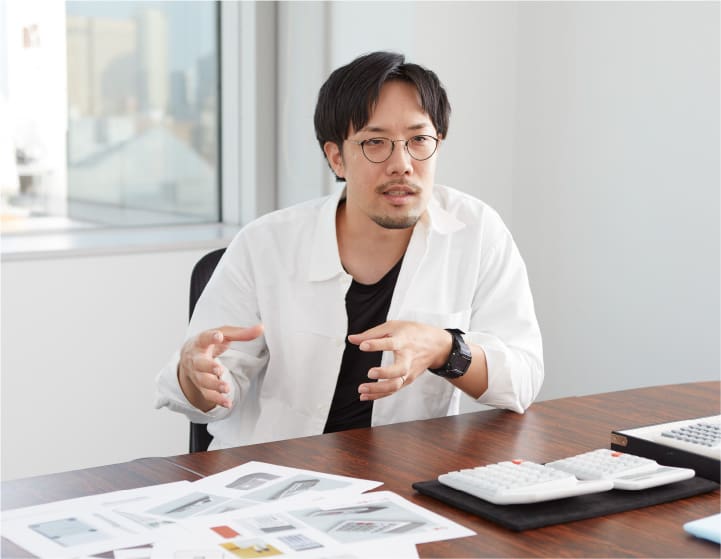 Product designer Shunsuke Oka sits at his desk and explains the ergonomic calculators in front of him