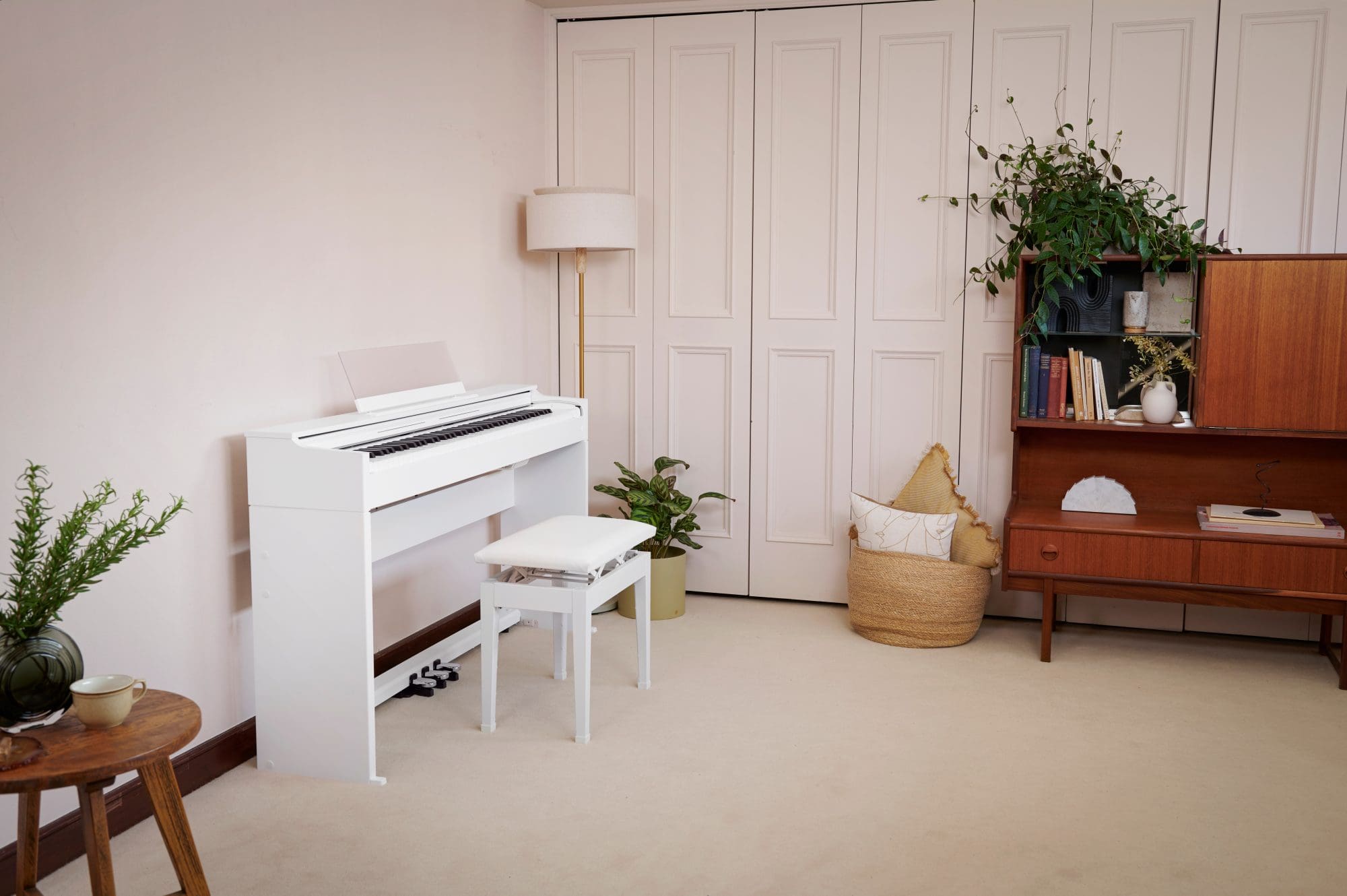 The white Celviano AP-S200WE on light flooring in a room with dark wood furniture and plants. Link opens the product page in the same window.