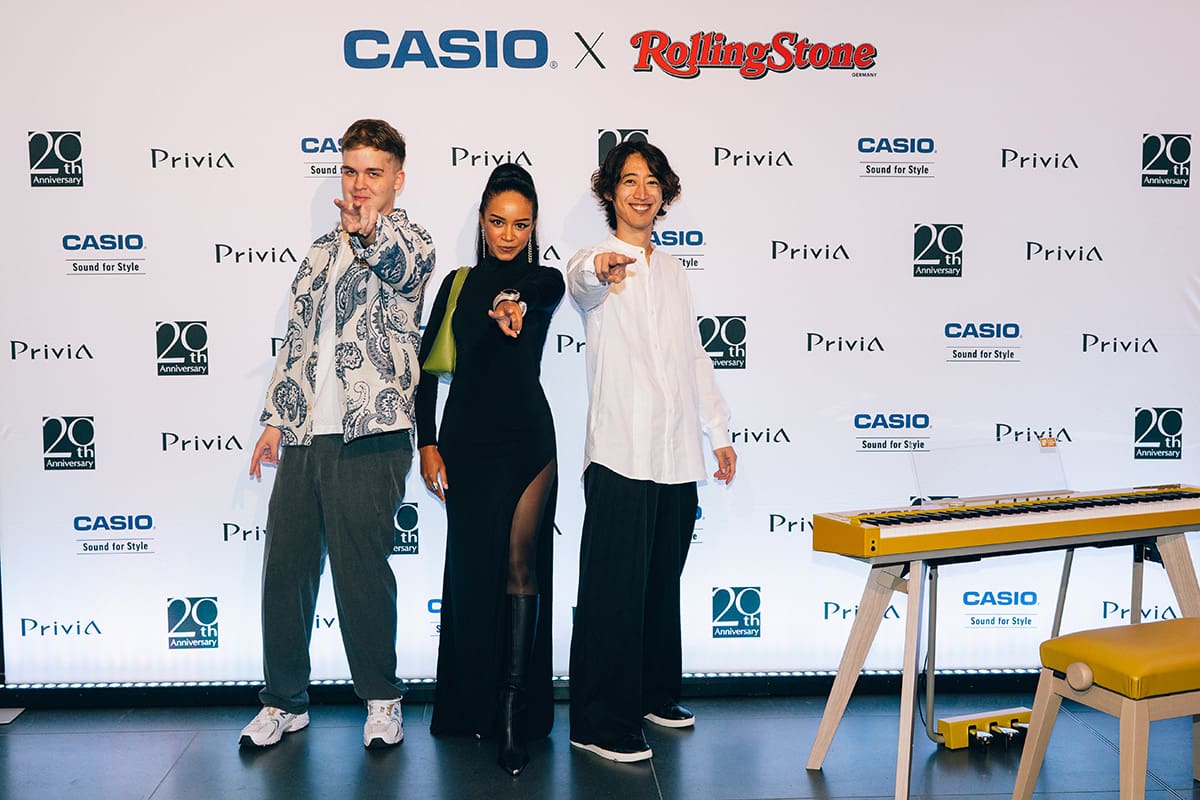 Levi Schechtmann, Imelda Gabs and Sumino Hayato stand together on a stage, with the Privia PX-S7000 in harmonious mustard on the right-hand side