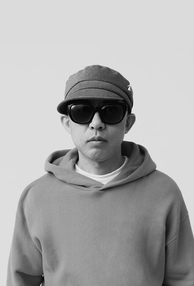 NIGO stands in front of the camera wearing sunglasses and a cap.