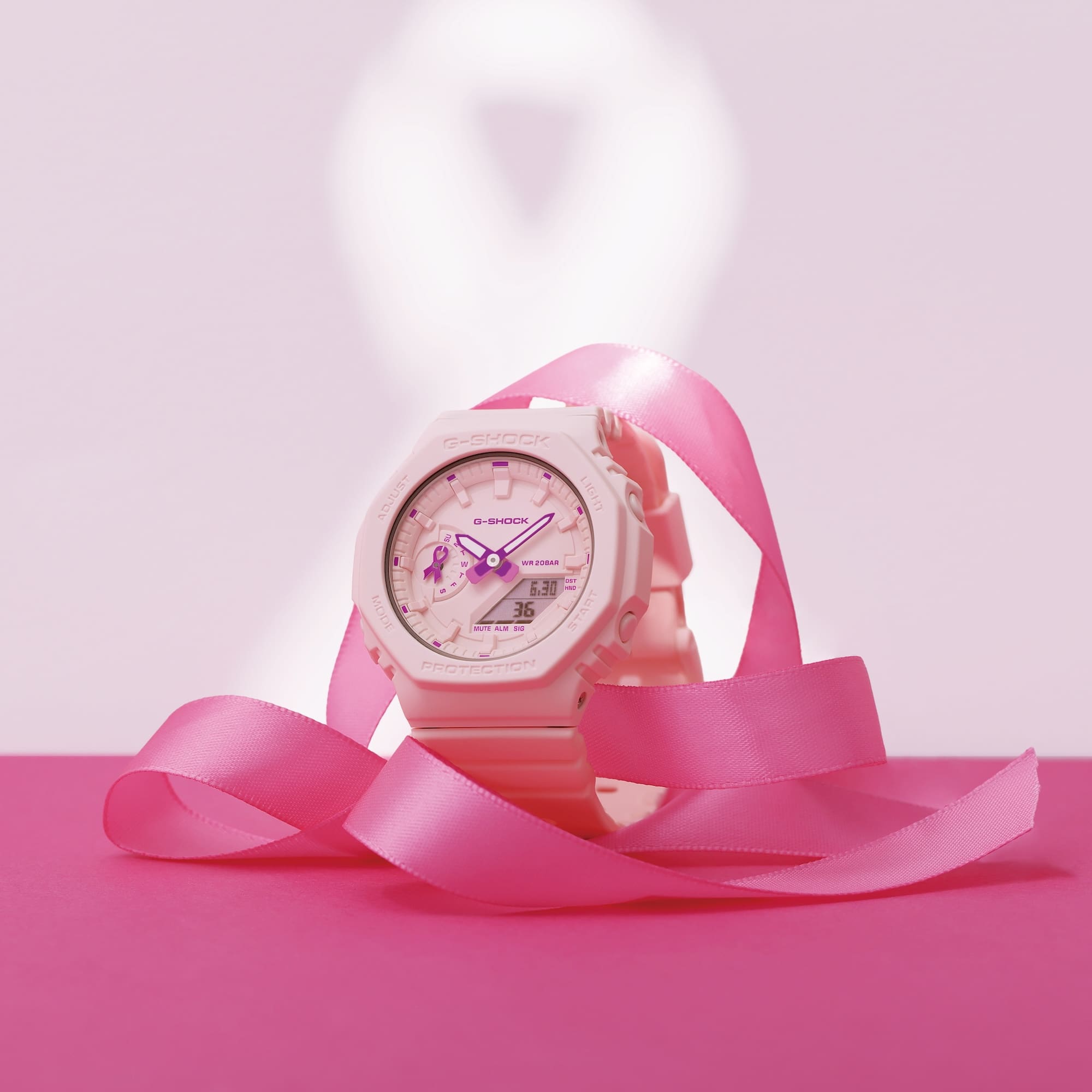 Die rosafarbene G-Shock GMA-S2100PR-4A umwickelt von einem pinken Band vor rosanem Hintergrund