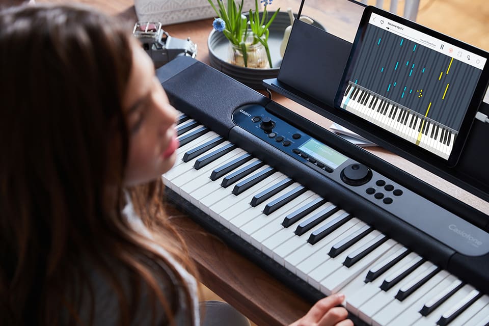 A girl sits at her desk and plays her keyboard with the piano roll function of the MUSIC SPACE app.