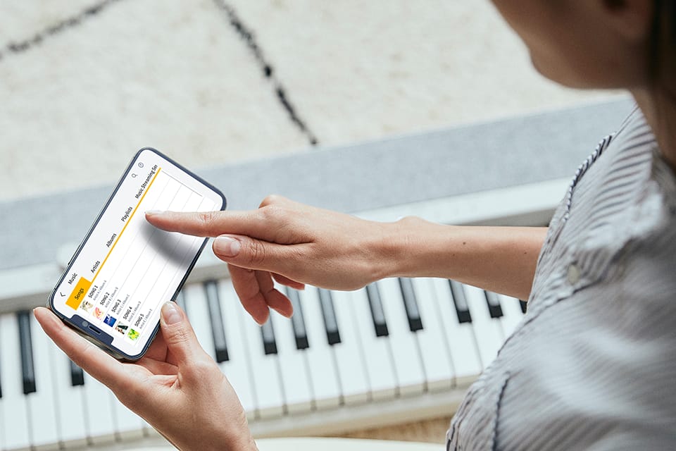 A woman selects a song in the app to practise on the keyboard.