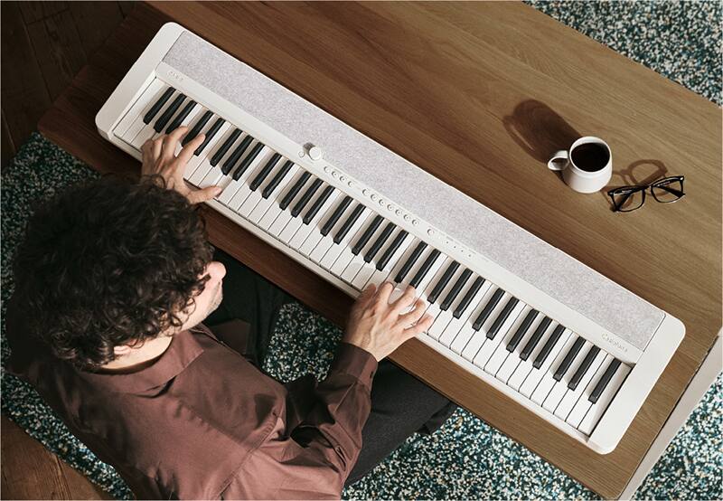 A man sitting at a wooden table playing the white CT-S1-76WE digital piano