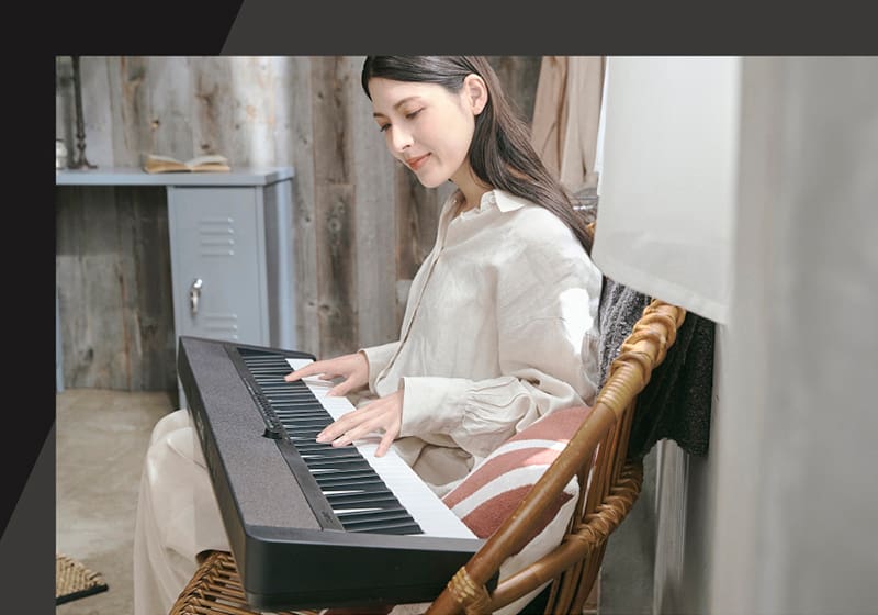 A woman is sitting on a wicker chair playing the black Casiotone CT-S1-76 in her lap