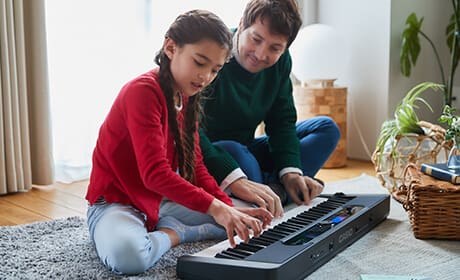 A girl is squatting on the floor next to a man, playing together on the Casiotone CT-S400 digital piano, which is lying on the floor in front of them