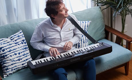 A man sits on a sofa and plays the Casiotone CT-S400 digital piano, which is placed over his lap