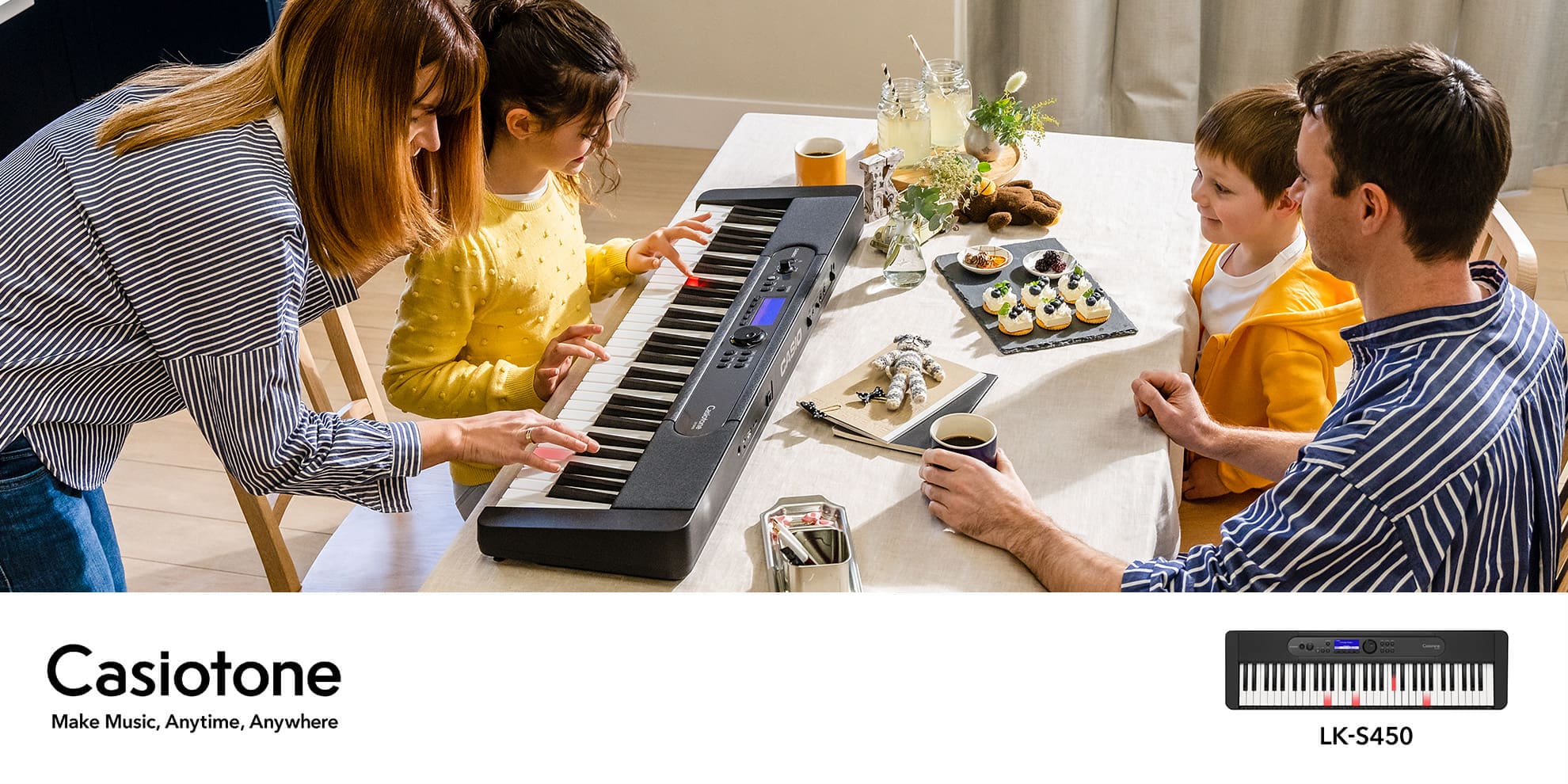 A girl is sitting at a table playing a Casiotone LK-S450 digital piano with her mother, while the rest of the family is watching.