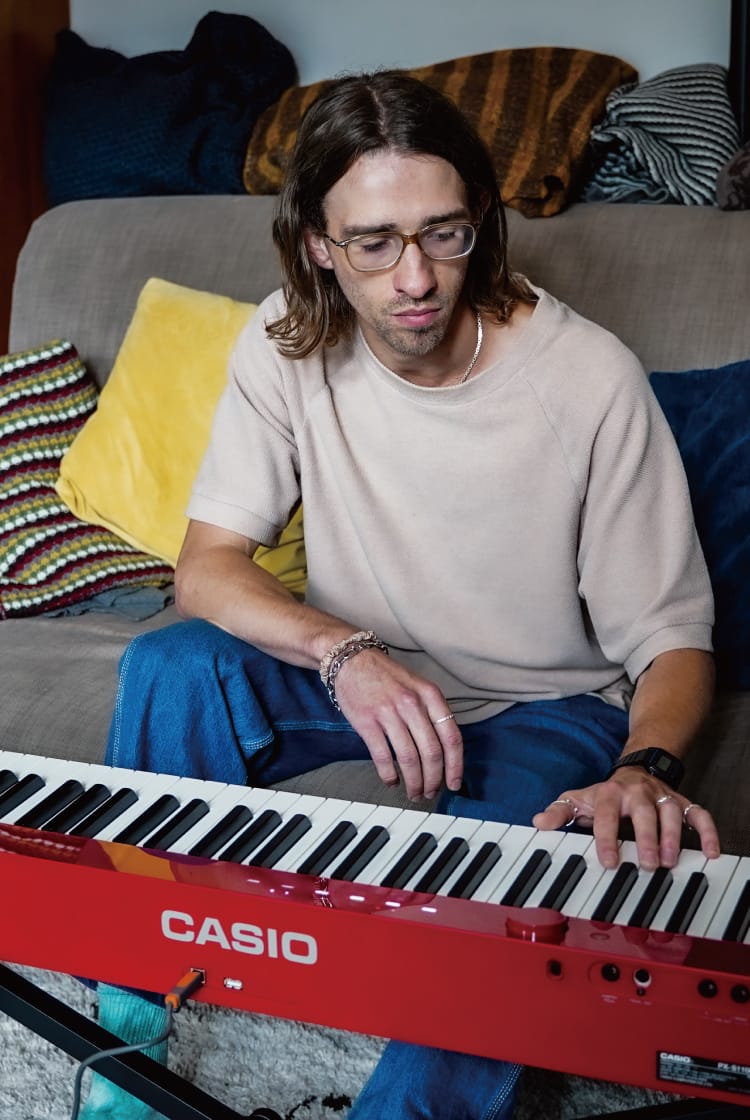 Joe Carver on the sofa in his London living room. His red Privia is on a stand in front of him. The picture links to his Life with Privia page.