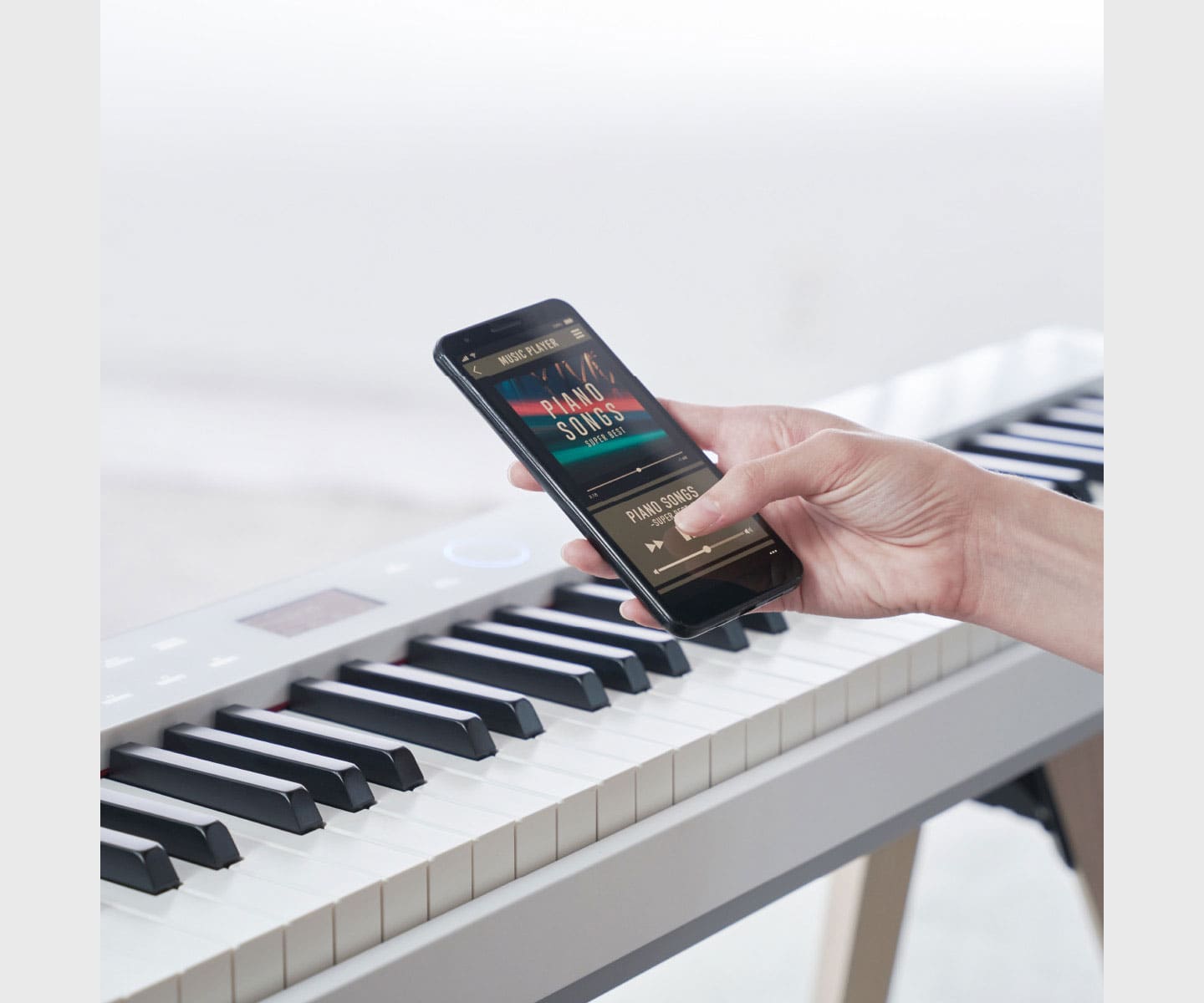 Someone operates the music player on their smartphone via the keyboard of a PX-S7000WE digital piano.