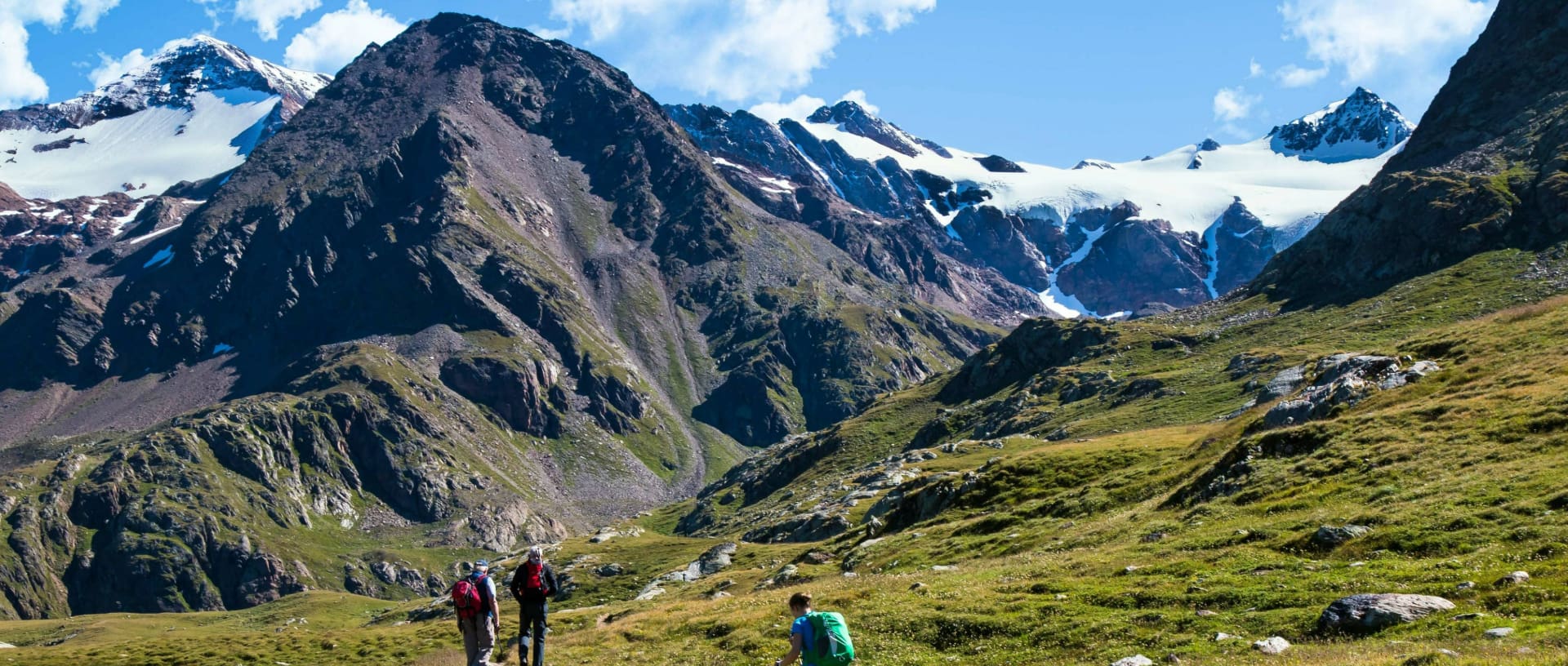 A few hikers in the mountains with snow-covered peaks in the background