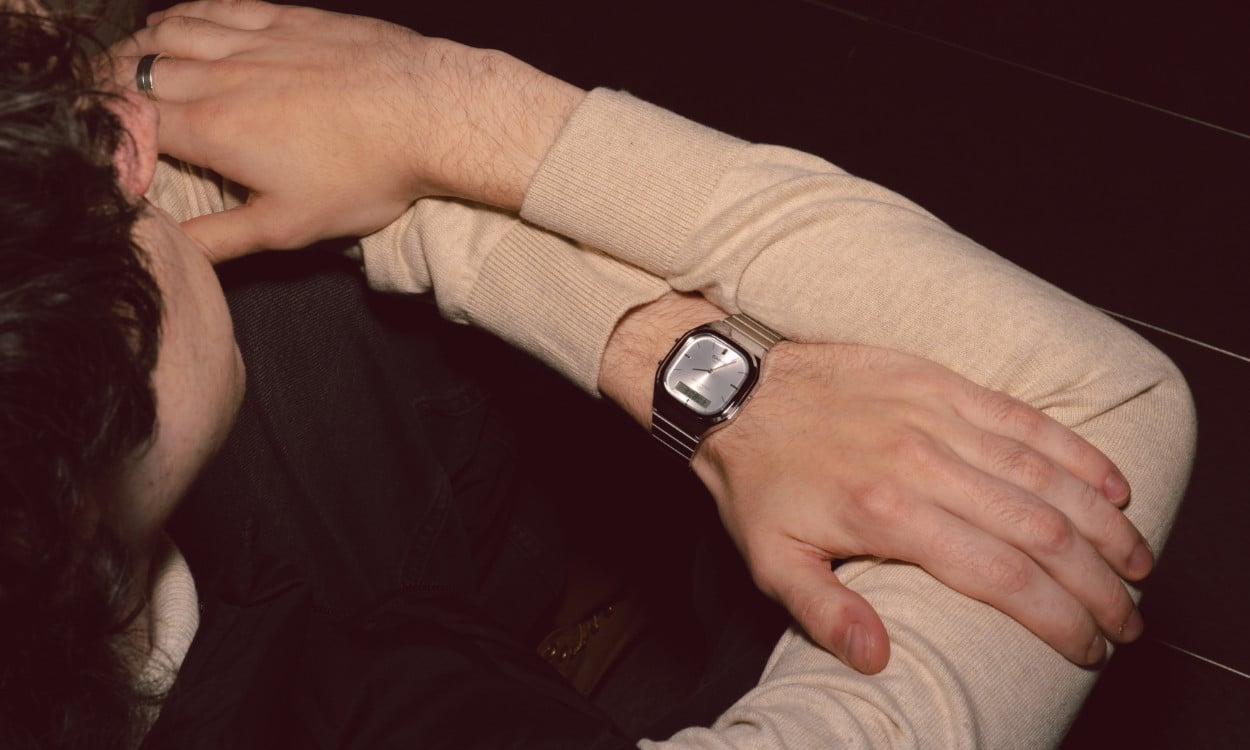 Close-up of a man from above wearing a beige pullover and the AQ-240E-7A on his wrist leaning onto a brown table