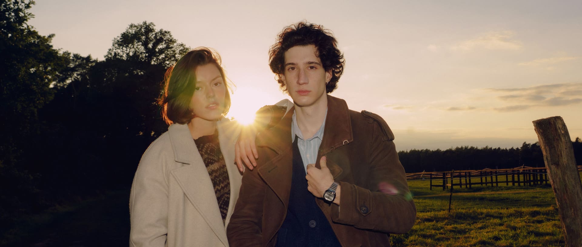 A couple walking outside on a field, she is wearing a beige coat, he is wearing a brown jacket, they are both wearing the AQ-240E watch models from the CASIO Vintage collection