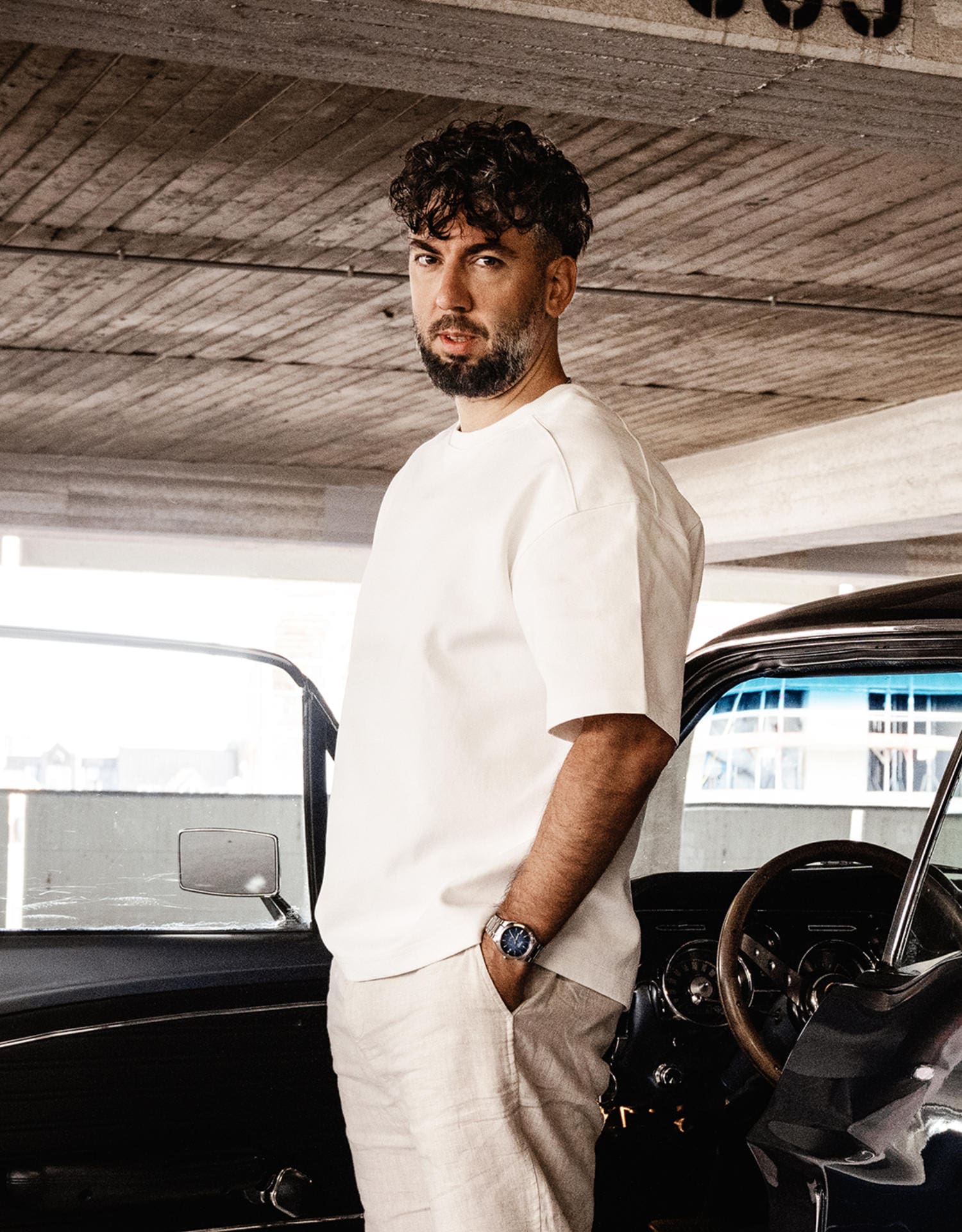 A man dressed in beige stands in front of a car in a multi-storey car park. On his wrist, he is wearing the silver and blue EFK-200D-2A wristwatch.