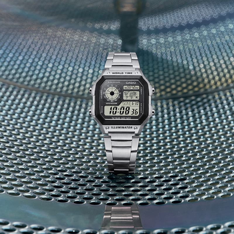The CASIO watch AE-1200WHD-1AV placed on a metallic surface in a laundromat setting.