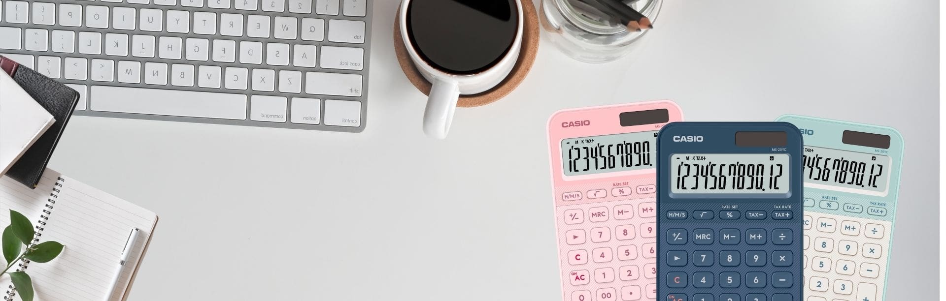 Deux calculatrices de bureau, l'une bleu foncé et l'autre rose, sont posées sur une table blanche à côté d'une tasse de café et d'un clavier.