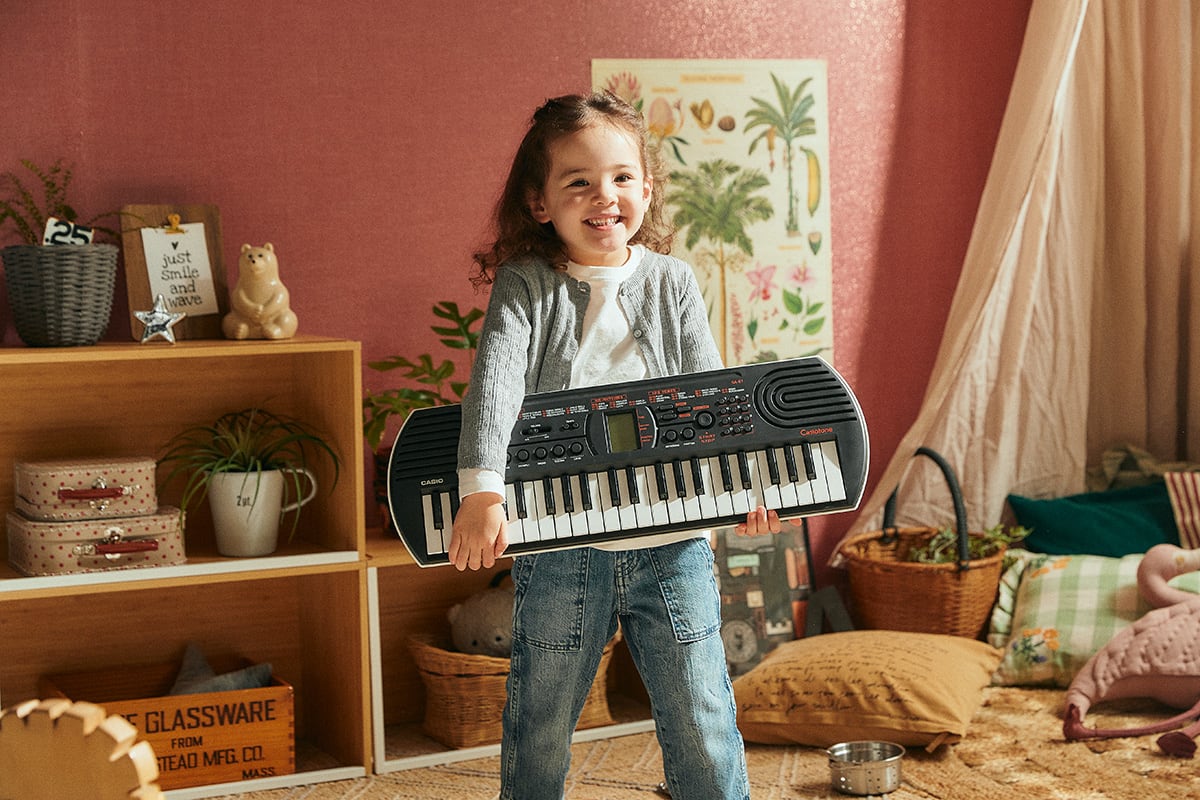 Une petite fille se tient dans sa chambre d'enfant et tient le clavier SA-81 dans ses mains en souriant.