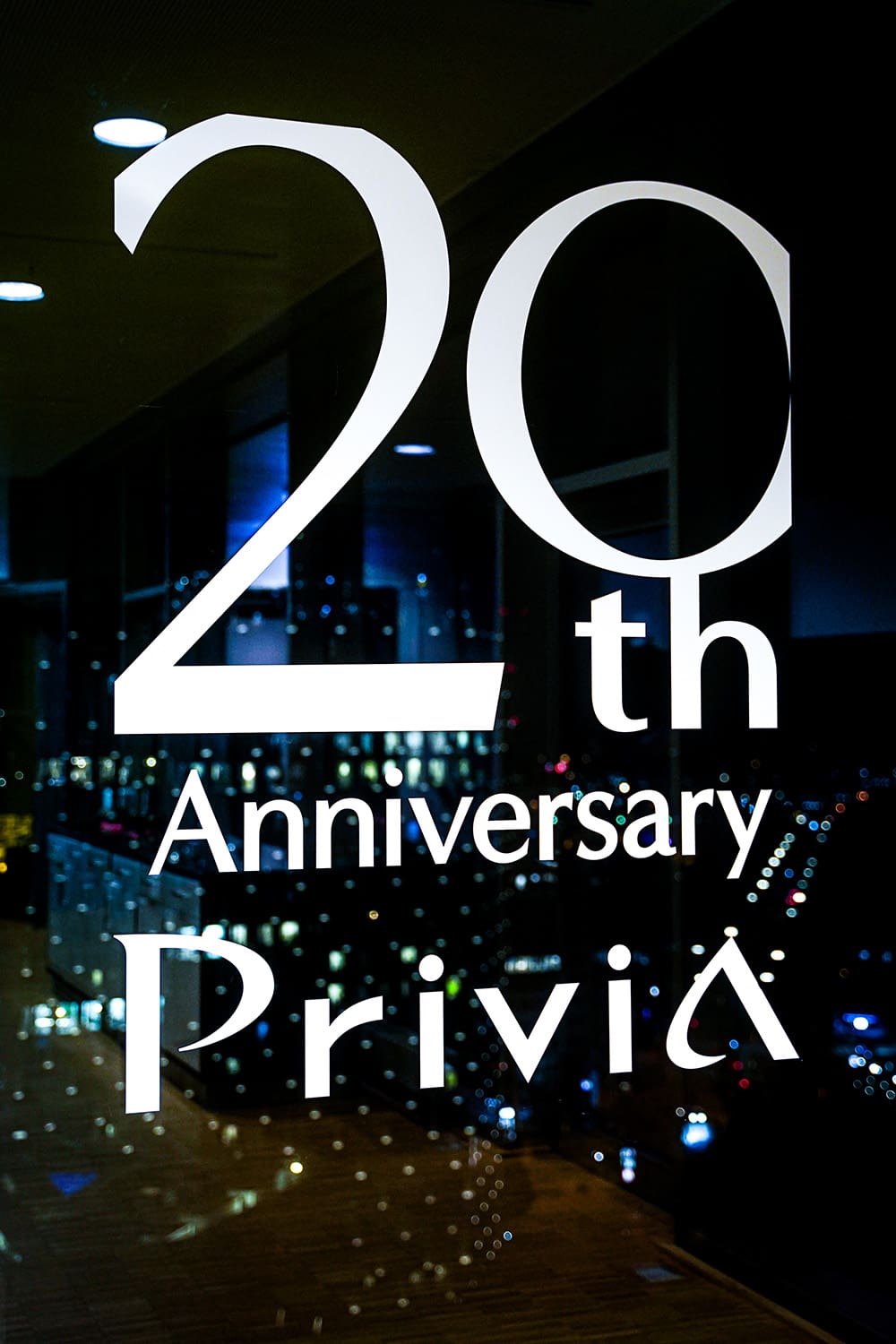 Lettrage « 20th Anniversary Privia » sur une vitre, avec un horizon urbain en arrière-plan.