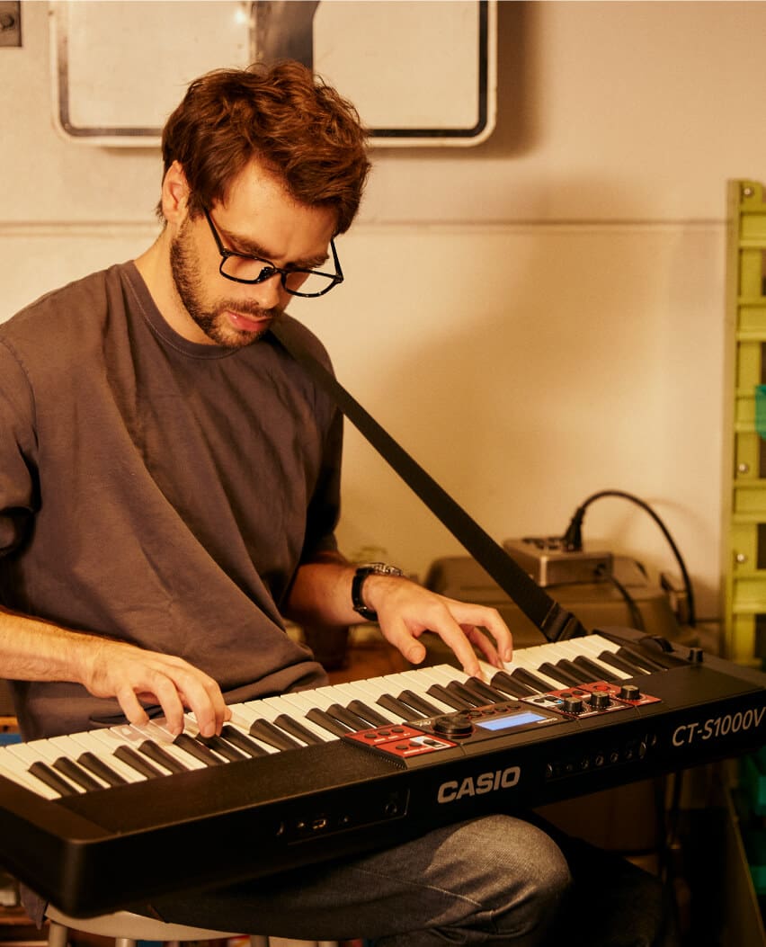Un homme joue du clavier posé sur sa cuisse. Il est maintenu par une sangle d'épaule.