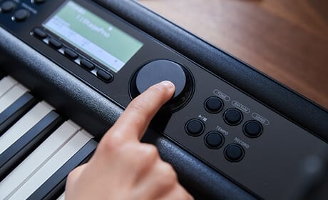 Un doigt actionne le bouton rotatif entre l'écran LCD et le clavier du piano numérique CT-S400 de Casio