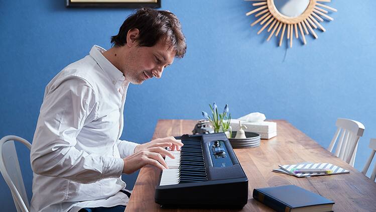 Un homme est assis à une table en bois et joue du piano numérique Casiotone CT-S400