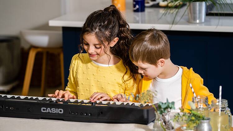 Une fille et un garçon sont assis à une table et jouent ensemble du piano numérique Casiotone LK-S450