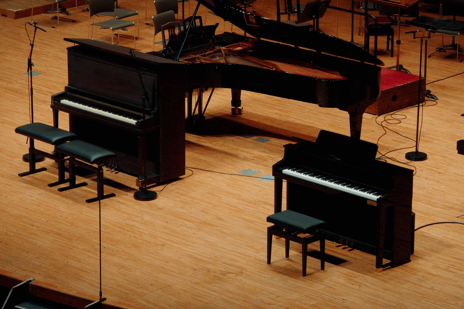 Deux pianos numériques noirs sur scène à côté d’un piano à queue et de micros