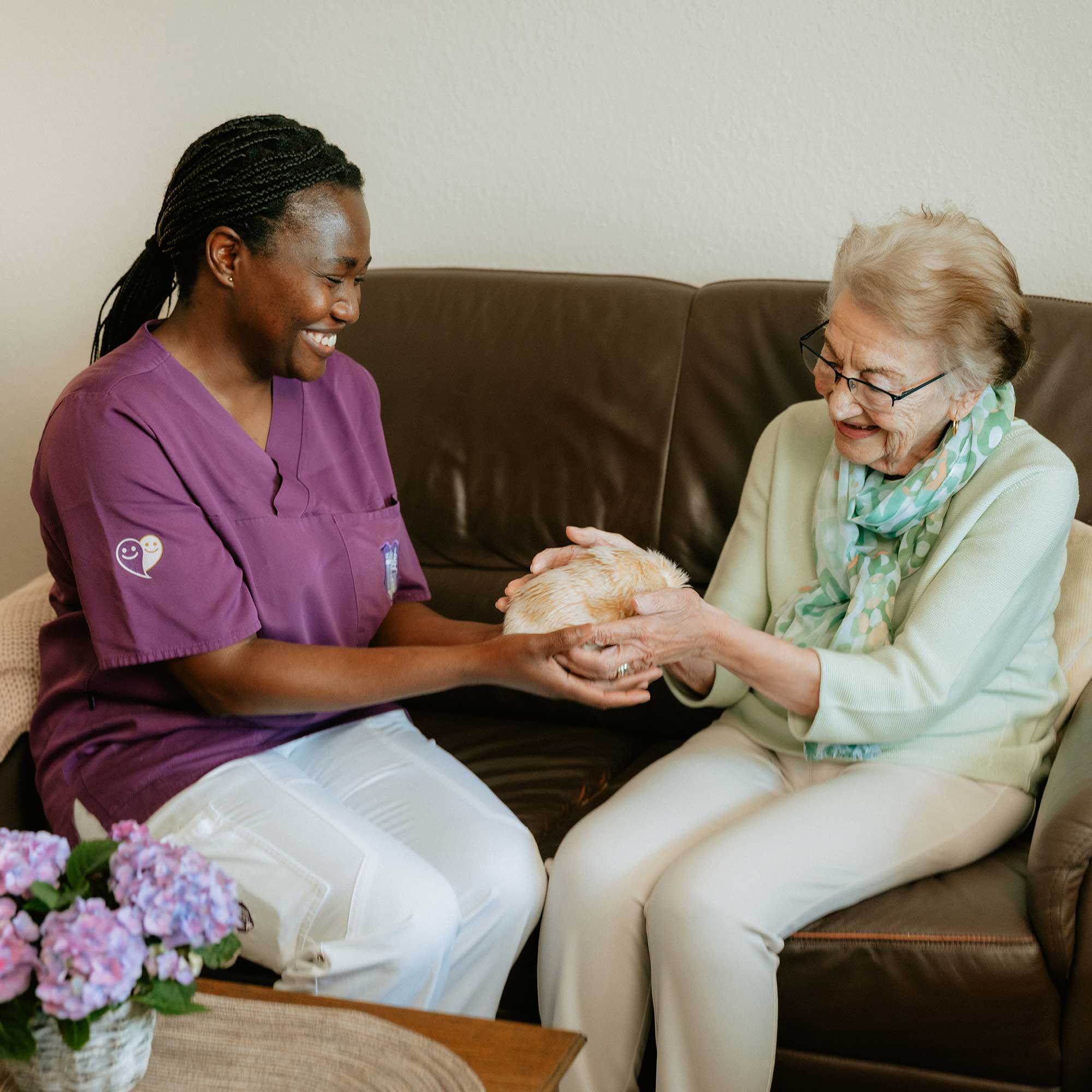 Une infirmière est assise sur un canapé avec une patiente et lui met un moflin dans les mains.