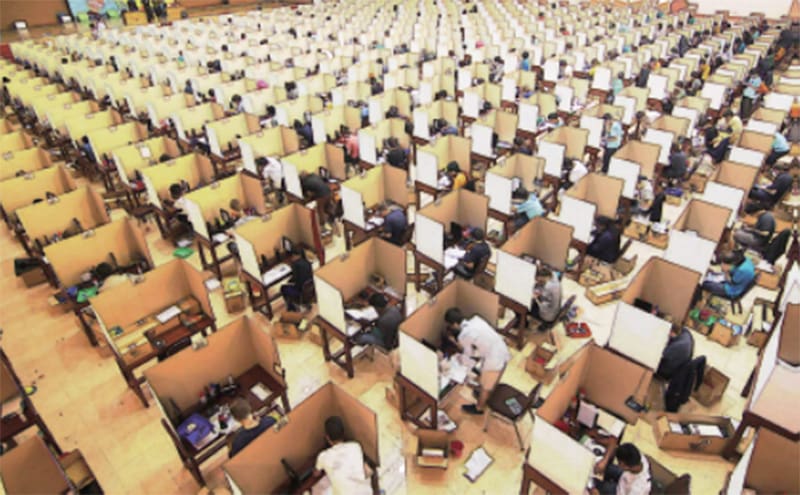 Examen : une grande salle avec des cloisons entre les différents bureaux et chaises où sont assis les participants aux Olympiades de physique.