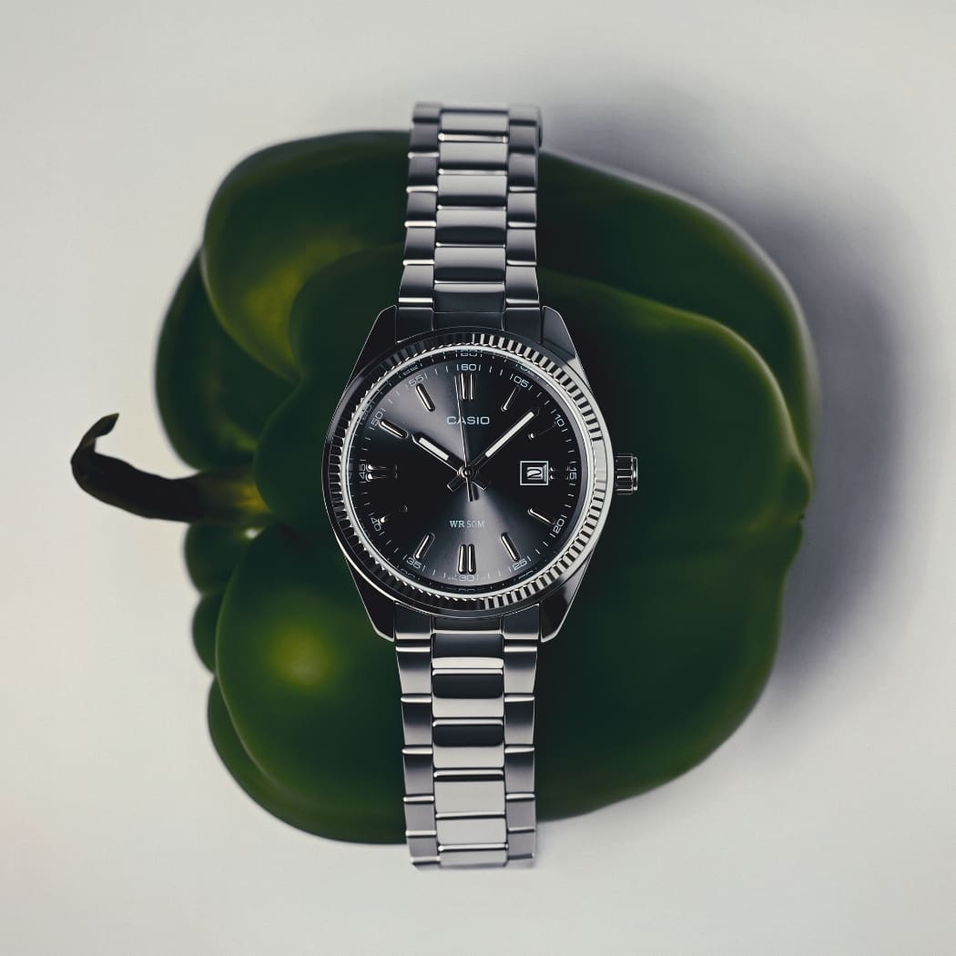 Montre CASIO Timeless 1302 à cadran noir et bracelet en acier, posée sur un support vert.