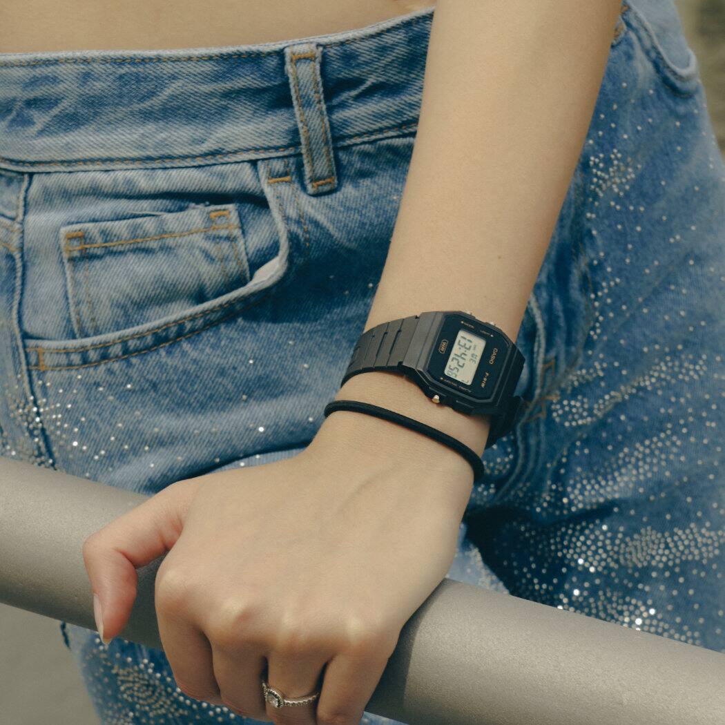 La montre F-91WB-8AEF avec un bracelet gris foncé au poignet d'un modèle féminin qui s'accroche à une balustrade.