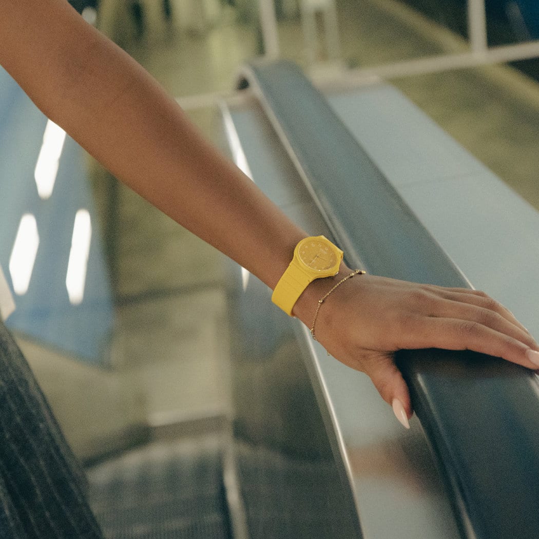 La MQ-24 au bracelet jaune et à l'affichage analogique au poignet d'une femme qui s'accroche à la rampe d'un escalator.