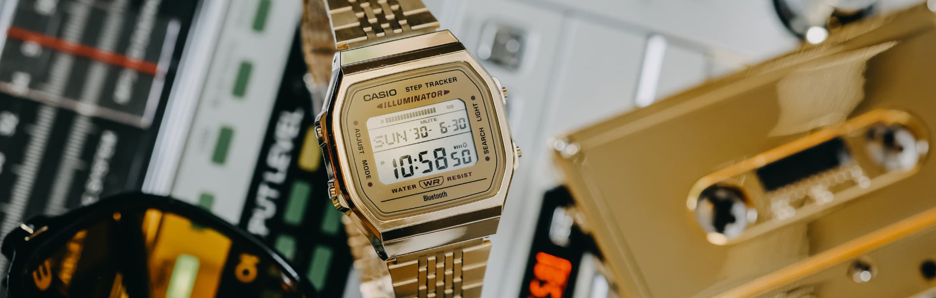La montre CASIO vintage ABL-100WEG-9AEF en or est posée sur un enregistreur à côté d'une caissette en or et de lunettes de soleil.