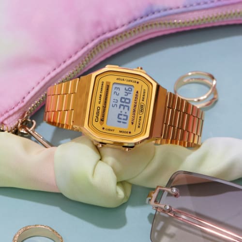 Montre Casio Vintage A168WG-9 en or à côté d'un sac rose et de bijoux en or