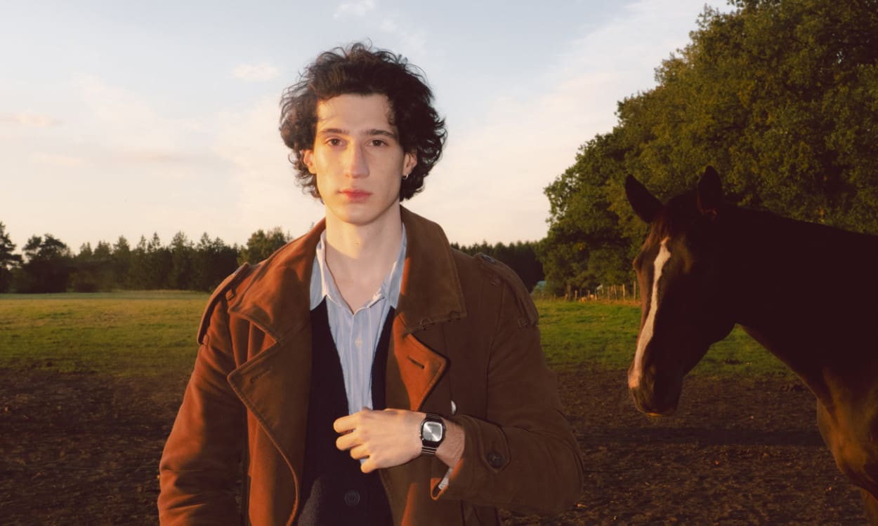 Un homme debout à l’extérieur près d’un cheval, portant une veste brune et la montre CASIO Vintage AQ-240E-7A.
