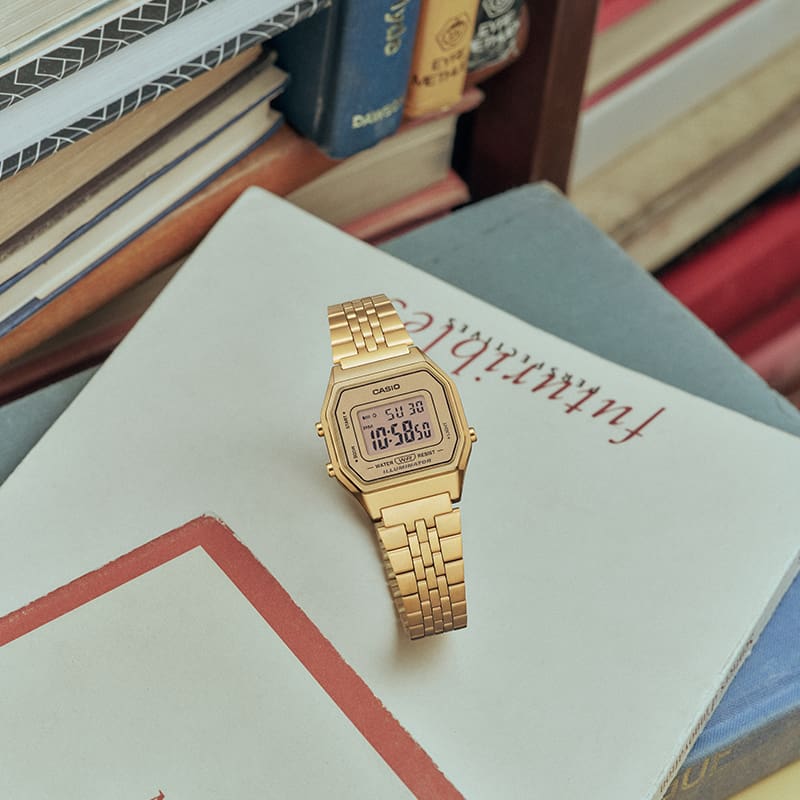 Photo de la montre numérique CASIO Vintage Collection LA680WGA-9 dorée sur une pile de livres.