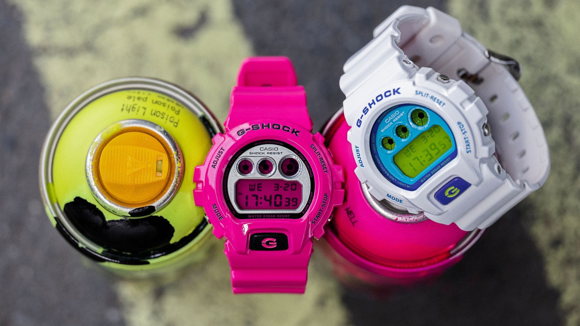 Les montres-bracelets G-Shock Crazy Colour blanches et roses sur des bombes de graffiti aux couleurs assorties.
