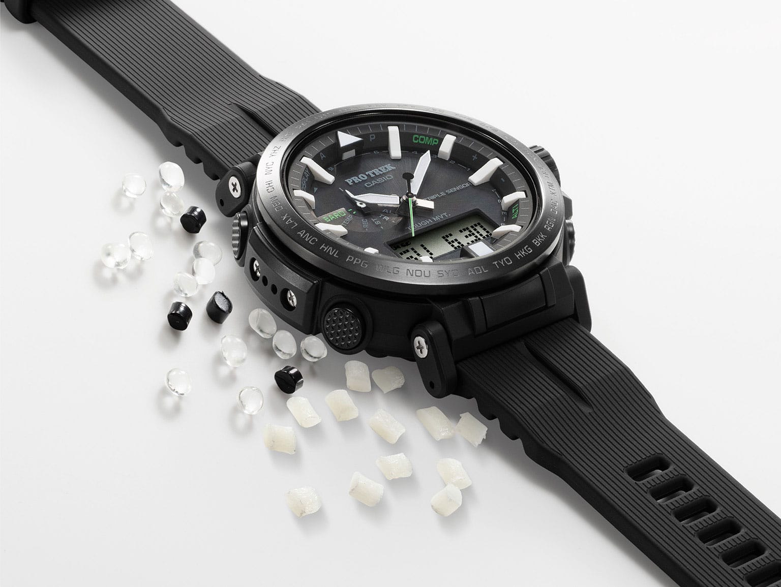 Une montre noire est posée à côté de pastilles noires, blanches et transparentes en résine bio.