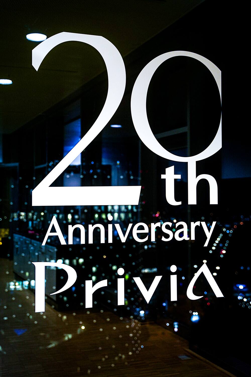 Scritta “20th Anniversary Privia” su una lastra di vetro, con lo skyline della città sullo sfondo