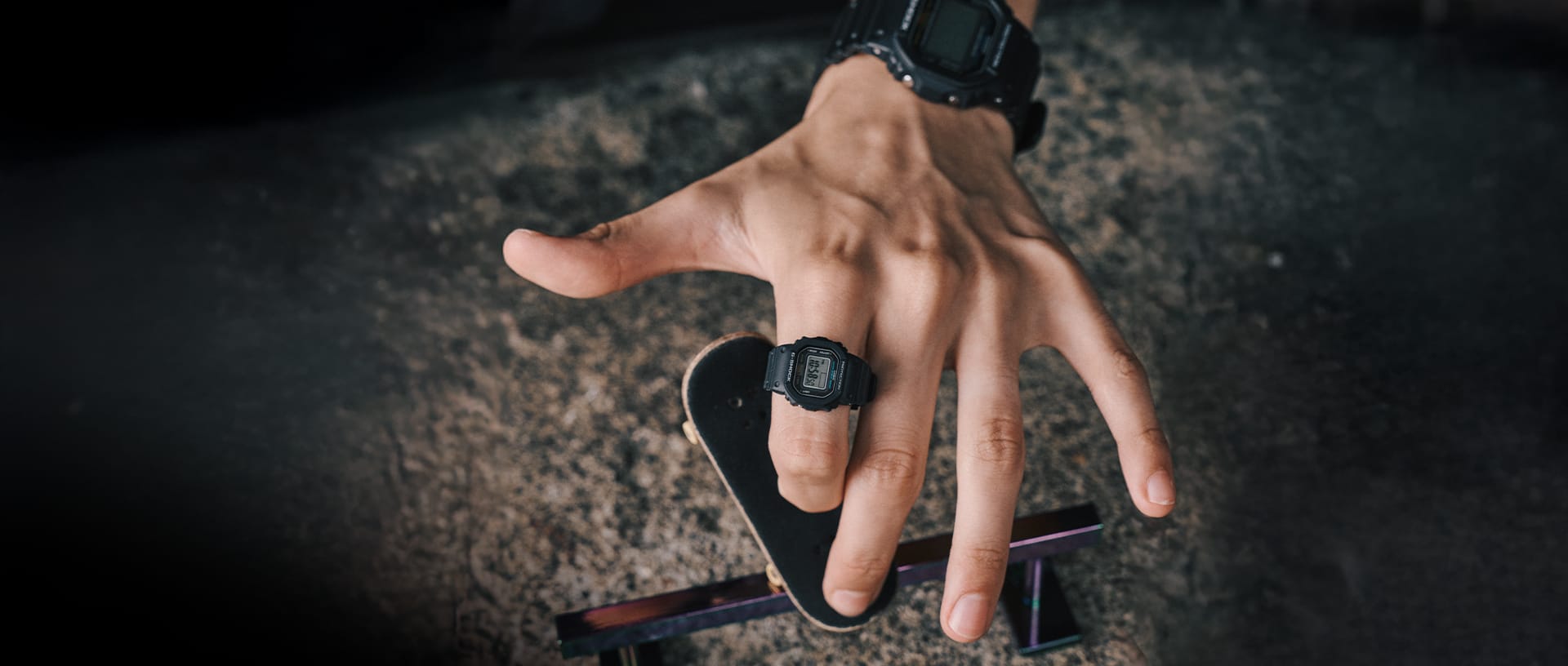 Una mano gioca con un piccolo skateboard e indossa l'orologio ad anello G-SHOCK in nero.