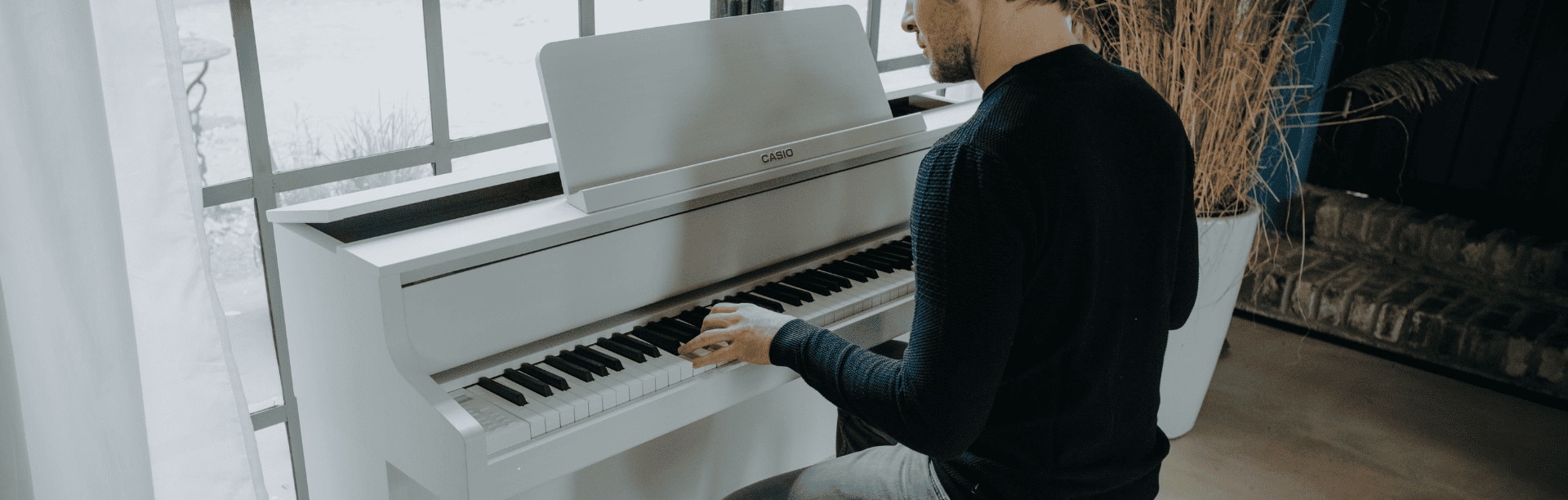 Un uomo suona l'elegante GP-310WE bianco davanti a una grande finestra. L'immagine rimanda alla pagina del prodotto del pianoforte digitale Celviano Grand Hybrid GP-310WE.