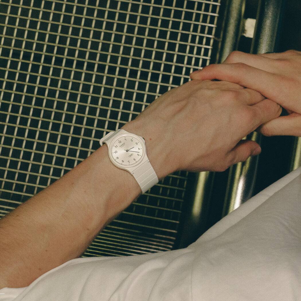 Un modello maschile si appoggia a una sedia e porta al polso l'orologio bianco CASIO TIMELESS COLLECTION MQ-24B.