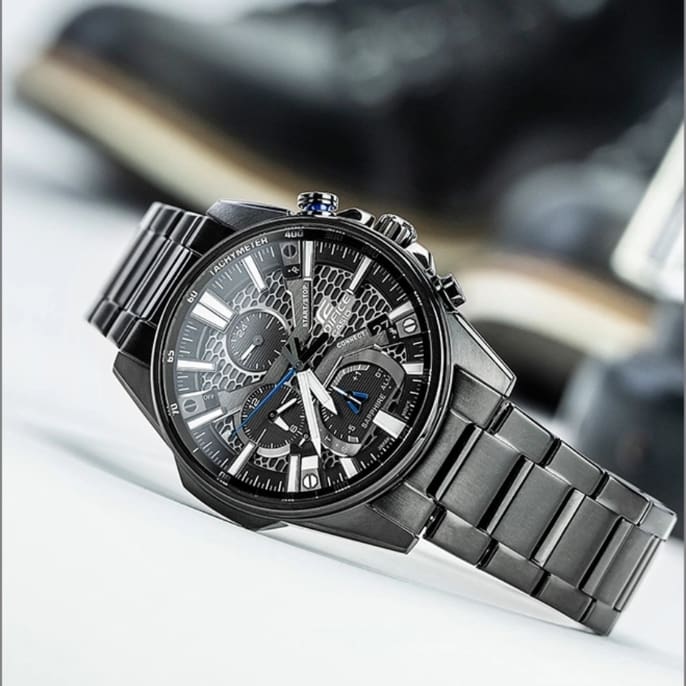 Il cronografo EQB-1200D-2A in argento con quadrante blu, indici bianchi e dettagli gialli appoggiato su un iPhone con custodia argentata