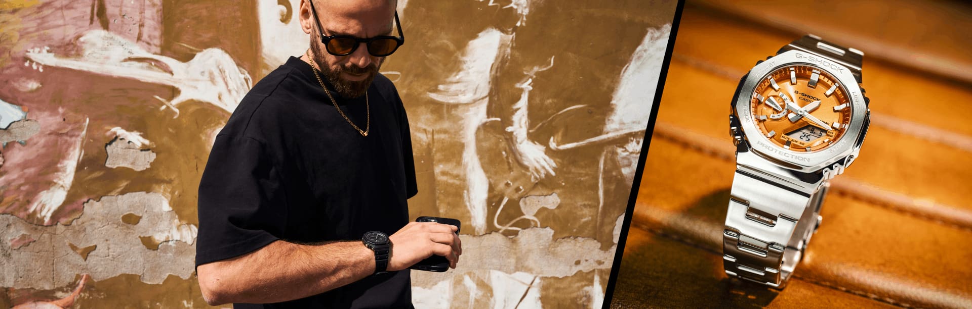 A sinistra un uomo in camicia nera con l'orologio da polso nero GA-2100 di G-Shock, a destra l'orologio in metallo argentato-arancione GM-2100 su una sedia in pelle.