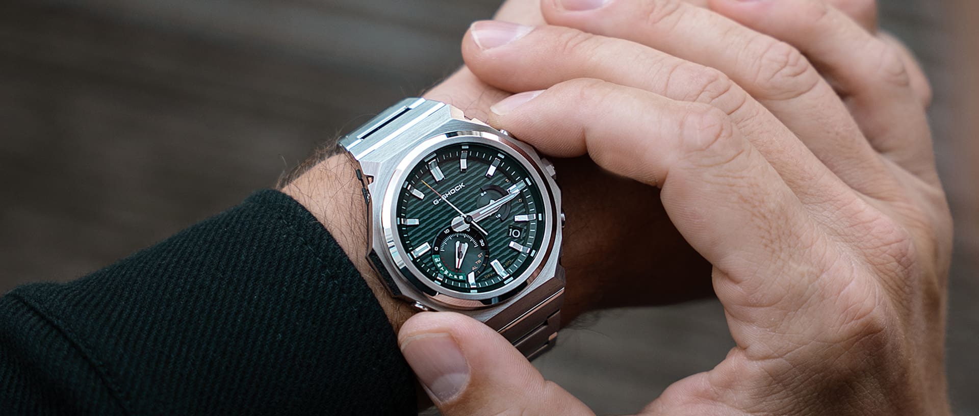 Primo piano del polso di un uomo che indossa l'orologio da polso GST-B1000 in argento  con quadrante analogico verde.