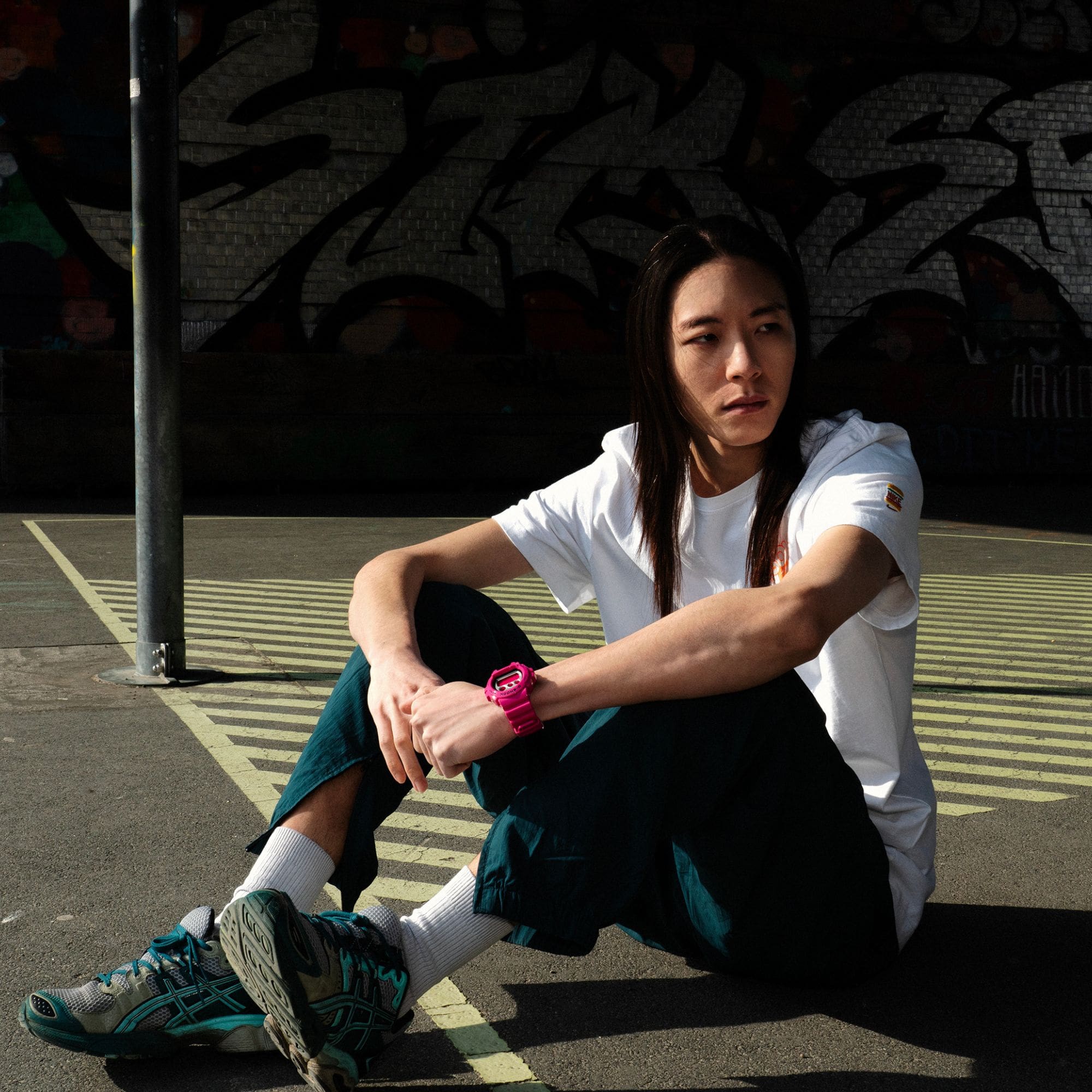 Una giovane persona con lunghi capelli sciolti è seduta su un campo da basket e indossa al polso il G-Shock DW-6900RCS-4 rosa. L'immagine rimanda alla pagina del prodotto.