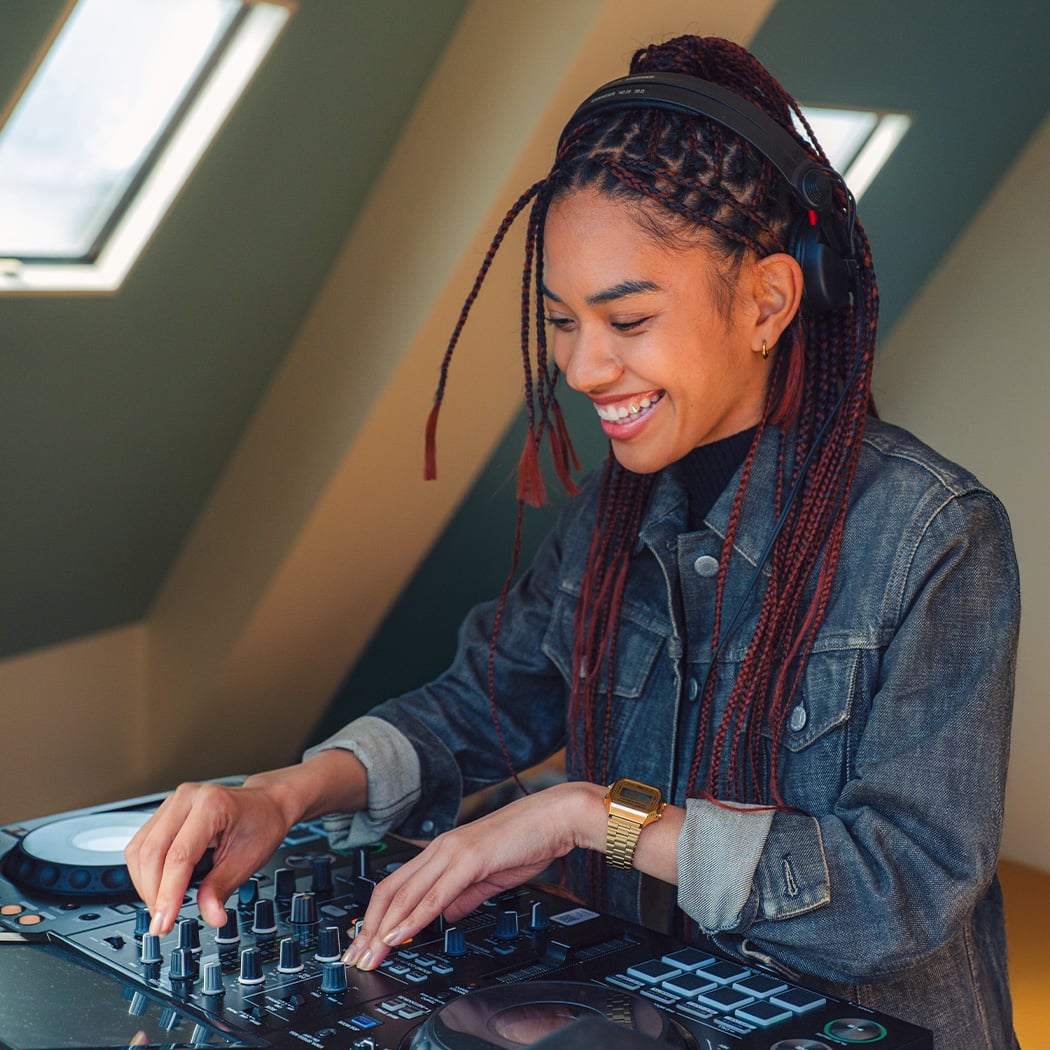 A woman at a mixing desk in a flat wearing a denim jacket and the A168WG-9 digital wristwatch in gold on her wrist