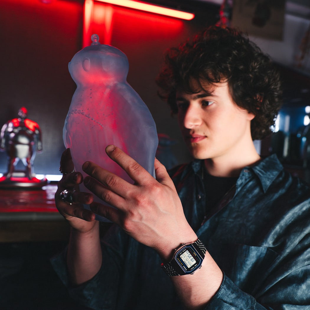 A man holds a figure in his hands, the digital watch ABL-100WE can be seen on his wrist.